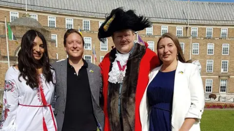 Antonina Grebeniuk Three people stand in front of the town hall with the mayor in full uniform