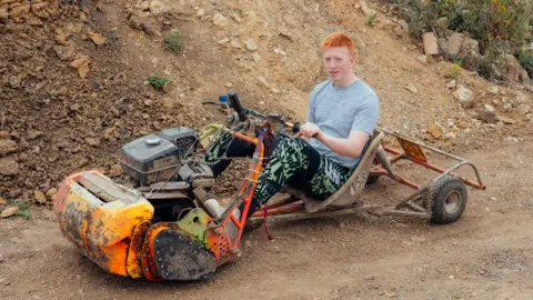 Harry George Hall A red-haired young man behind the handlebars of a modified lawn mower 