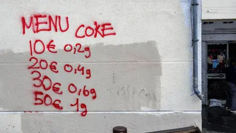 AFP via Getty Images Esta fotografia de 3 de dezembro de 2025 mostra pichações indicando preços de medicamentos na parede da torre Bell Horizon, no 3º arrondissement de Marselha.
