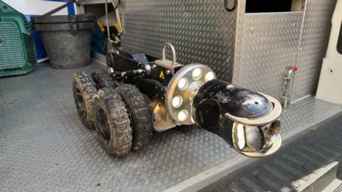 An eight wheeled robot which has a camera on the front and lights. the camera can be moved up and down. the robot goes up and down sewage pipes to inspect them.