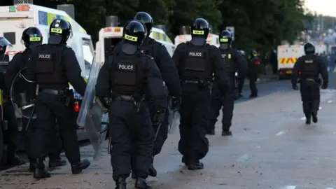 The back of riot police in full uniform including helmets and shields.