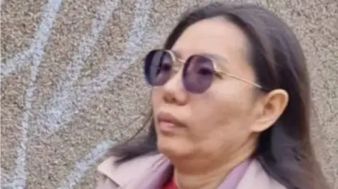 A 40-year-old Thai woman with sunglasses and a pink coat stares straight ahead 