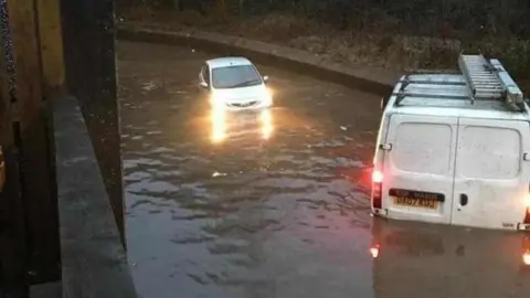 Paul Thomas A white van and a silver car, part submerged in dirty water which floods a residential street.