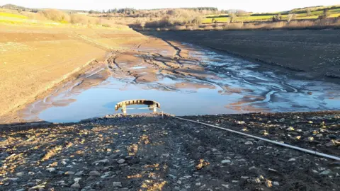 The drained Clypse Reservoir, which has a muddy bottom and steep embankments on either side.