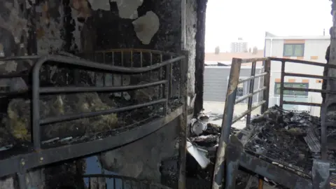 Tower Hamlets Council The burnt interior of one of the rooms, with multiple charred metal bed frames. 