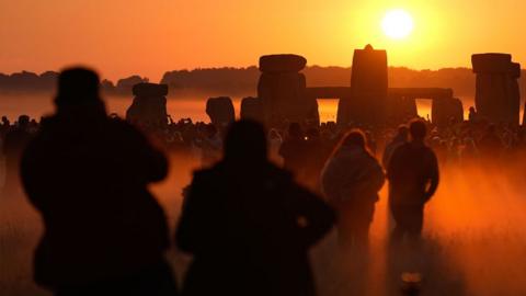 People watch the sun rise, as they take part in the Summer Solstice at Stonehenge in Wiltshire on 21 June 2024