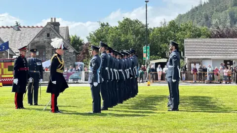  The lieutenant governor in full ceremonial dress standing in front of the Guard of Honour, which is lined up in two rows and standing to attention. 