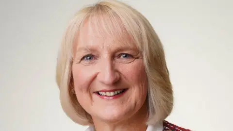 CJI A close-up image of Jacqui Durkin. She is an older woman who has short, blonde hair and she is smiling at the camera. She is placed against a white background.