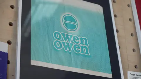 A framed paper bag from Owen Owen. It is light green and features a distinct design. 