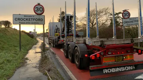 A lorry approaches the village of Crocketford which has a sign asking people to "please drive carefully" and a 30mph speed limit above it