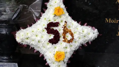 Getty Images A bouquet of white flowers in the shape of a cross, with the number '56' emblazoned in claret and amber in the middle.