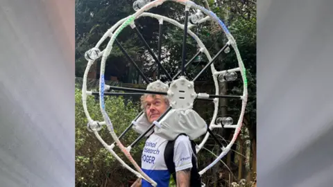 Roger Farnsworth A man in running gear with a miniature big wheel resting on his shoulders