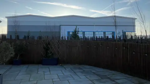 Dave Gerrard Warehouses can be seen towering over a garden fence. 