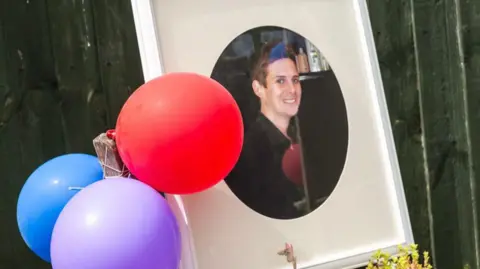 Dorset Bays Photography Three balloons are tied beside a photo frame featuring a photograph of a smiling young man dressed a black shirt