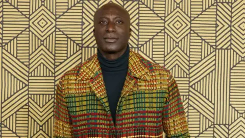 A head-and-shoulders shot of Ozwald Boateng wearing a colourful woven coat. 