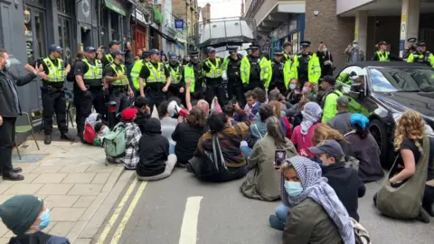 BBC People sitting on the street in front of police