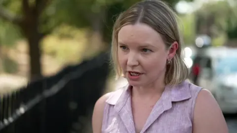 A young woman with brown hair standing in the street being interviewed for TV. 