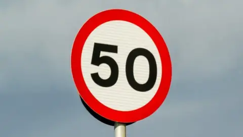 A 50 speed limit sign in black lettering surrounded by a red circle.