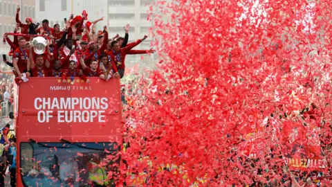 Reuters Red confetti in the air in front of the Liverpool bus in 2019. Players raise their arms in celebration on the open-top bus.