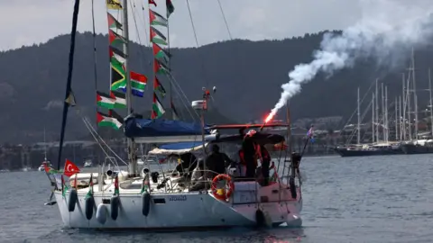 Reuters Activists on board a sailboat taking part in the Global Sumud Flotilla light flares as they depart from the port of Marmaris, southern Turkey (14 May 2026)