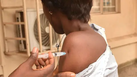 A nurse injecting the arm of a health worker in West Africa with Ervebo - archive shot