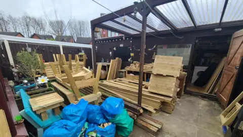 Bob Williams A range of wooden products are piled up outside a large brown shed with a covering over the front