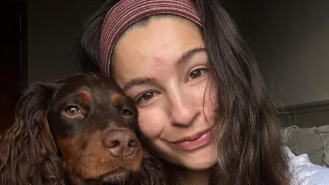 Betty Mukherjee A woman wearing a maroon‑and‑white striped headband leaning closely beside a brown dog with wavy fur and tan markings.