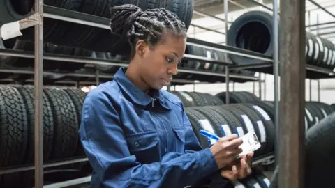 A woman at work ticking off a list with tyres behind her