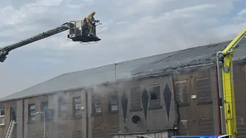 Lancashire Fire and Rescue Service A firefighter in a cherry picker holds a hose above the smouldering roof of the club.