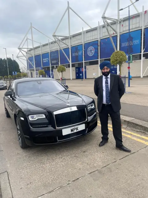 Morgan, Payne & Knightly Tony Singh is wearing a business suit and a turban. He is standing in front of Leicester City Football Club. Behind him is a luxury car with the number plate MPK. 