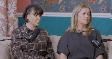 Lime Pictures Two women - Alex Fletcher and Jessica Fox - are sitting on a couch with microphones in front of them. The room is decorated with brightly-coloured floral wallpaper. 