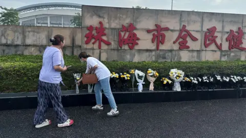 Reuters Two women lay flowers outside stadium in Zhuhai after attack