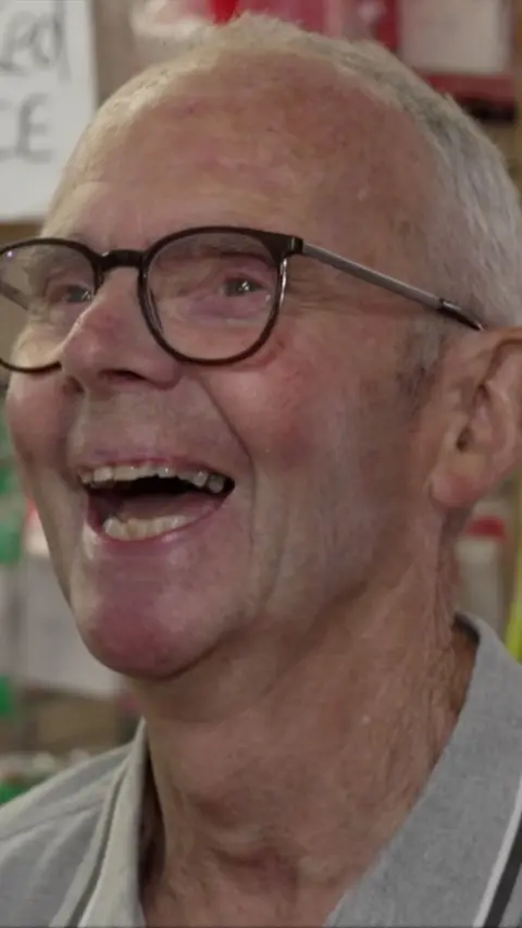 Patrick Meredith, he's a white man with glasses and grey hair. He's mid laugh, looking just away from the view of the camera.