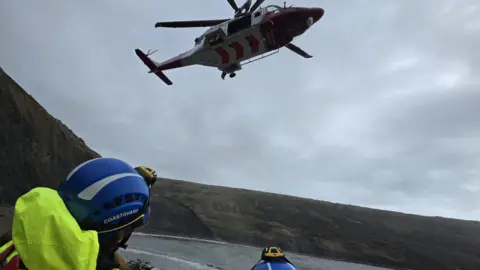 Coastguard teams at a cove with a helicopter above.
