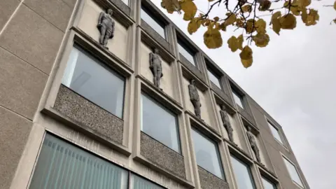 Lara King/BBC An imposing grey library building with friezes of figures in between rows of windows.