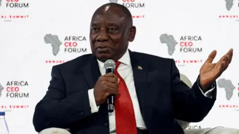 Reuters President Cyril Ramaphosa wearing a black suit and a red tie speak at a forum