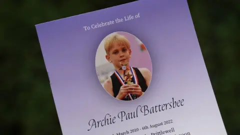 PA Media Archie Battersbee order of service for funeral, paper is gradient purple colour with an image of Archie holding a trophy at the top.