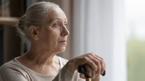 Getty Images older woman sitting with her hands on a cane