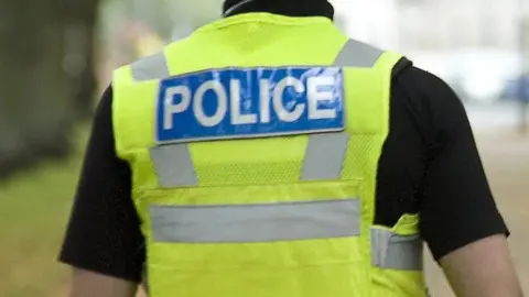 PA Media A generic image of a police officer seen from the back. He is wearing a dark short-sleeved shirt and a yellow hi-vis vest with the word "POLICE" on its back in blue and silver.