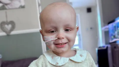 A two-year-old girl with a hospital tube through her nose.