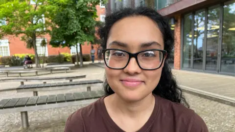 BBC Shahama is 18 and is smiling. She wears glasses and has black curly hair.