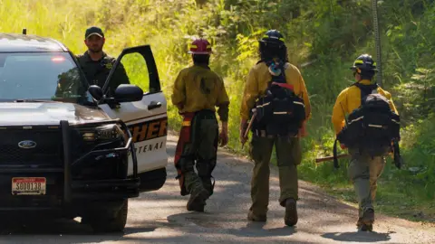 Firefighters walking along a road with a police officer getting into a car