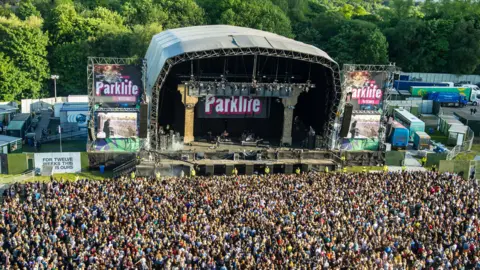 Parklife crowds from file photo in June 2015 of the site on day 2 of the Parklife festival in Heaton Park. Thousands of revellers can be seen in front of a stage saying Parklife on it. several vans and trucks can be seen behind it. 