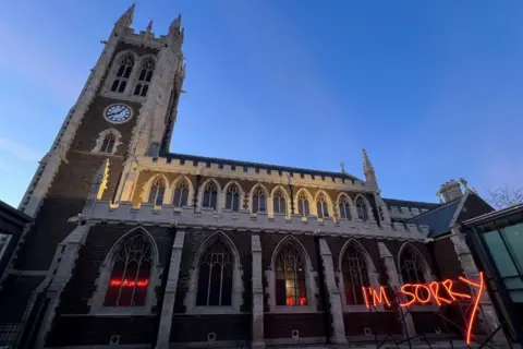 Annabel McCourt A church at night with large neon lettering in red outside saying "I'm sorry".