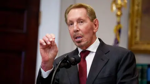 Oracle co-founder Larry Ellison gesturing while making a speech before a microphone