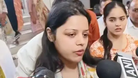 Himanshi Narwal is talking to media persons. Her hair is open and she is wearing an mustard kurta with a printed dupatta. 