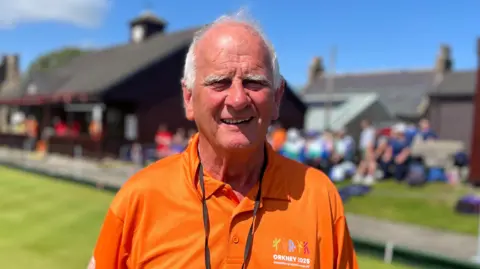 Man wearing orange top, with blurred bowling green in the background