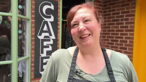 Lisa who is smiling is wearing a black apron