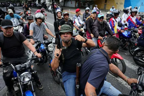 Getty Images A large group of people on motorcycles, some of them armed. One mand holds a rifle and grimaces at the camera, his other fist clenched.