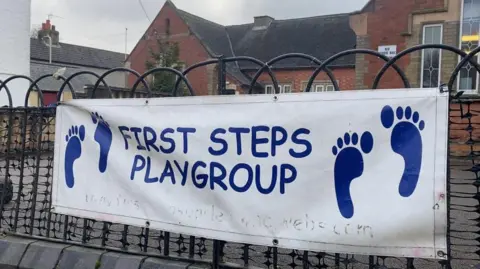 A white banner with blue text spelling First Steps Playgroup